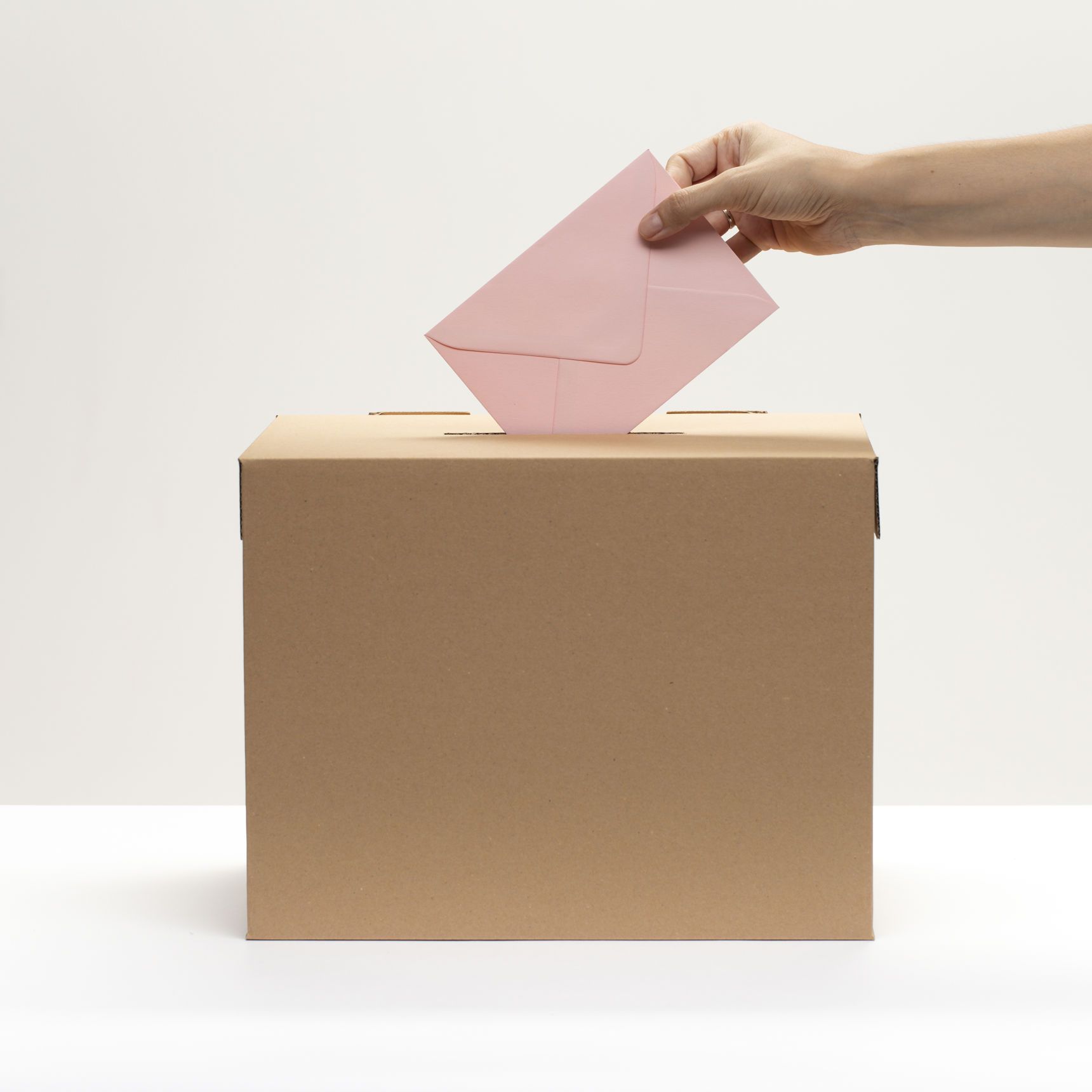 En kvindelig hånd putter en konvolut i en stemmekasse