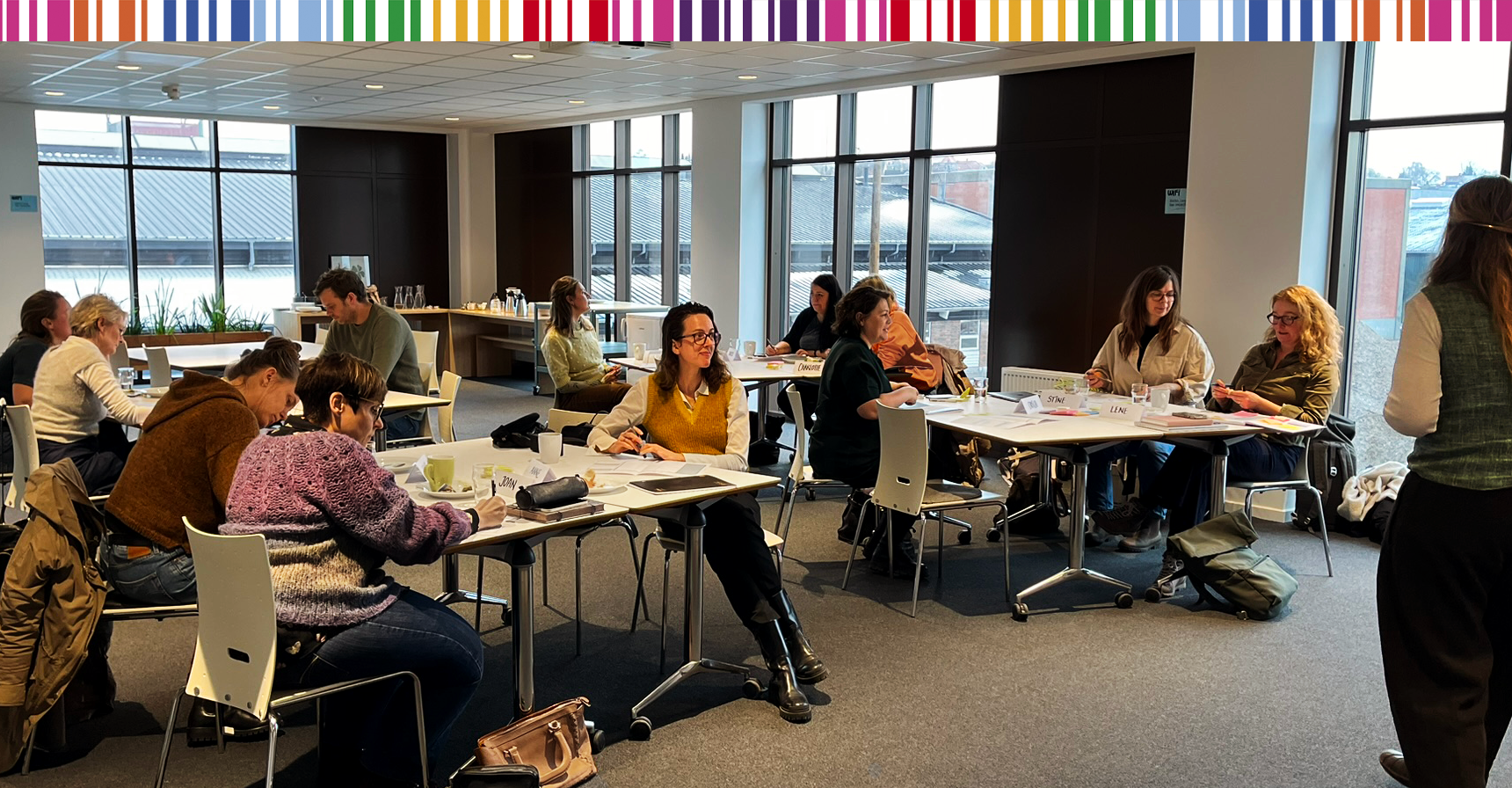 Kvinder og mænd ved borde i et mødelokale